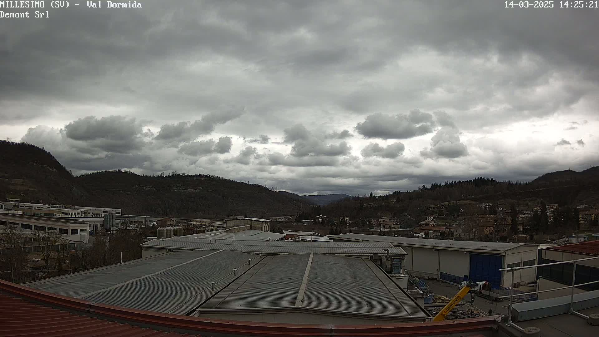 Overcast skies hang above a valley of industrial buildings and residential homes nestled between hills.