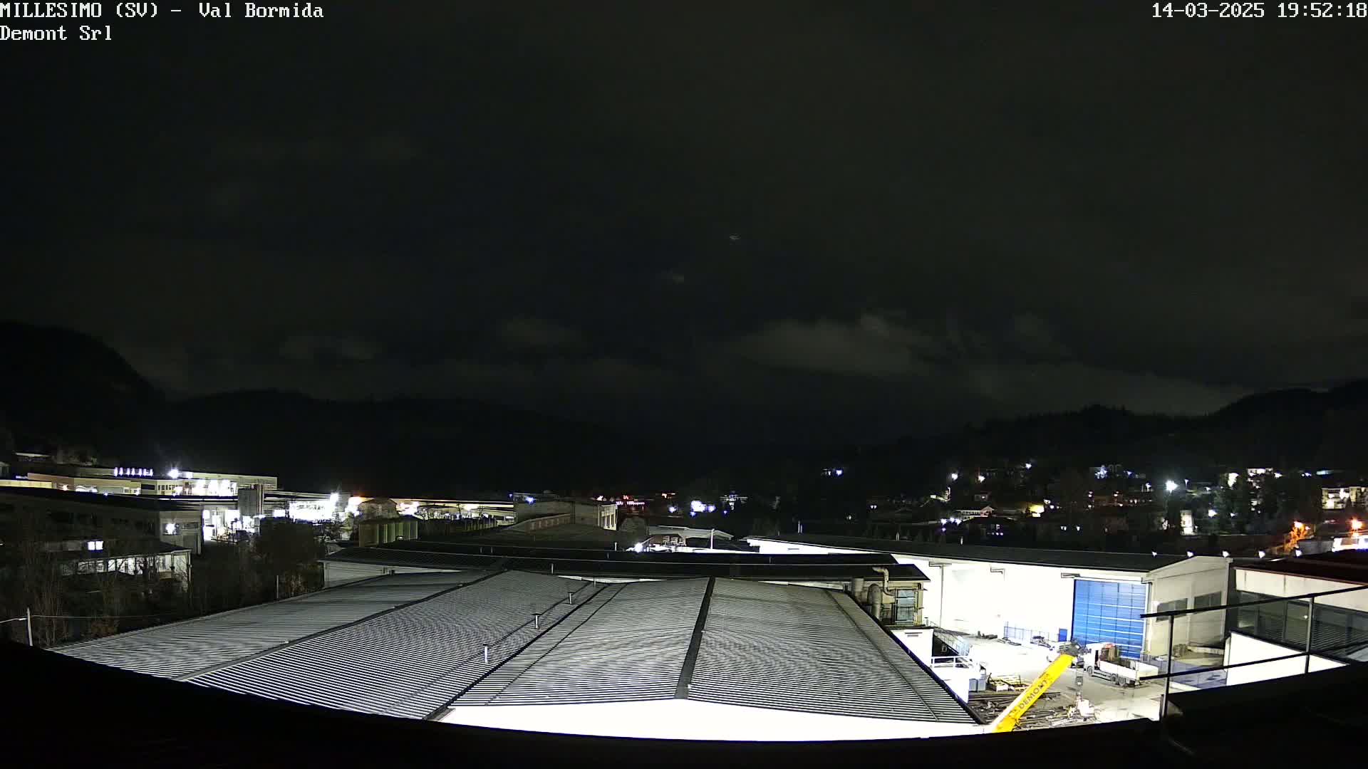 A nighttime view of an industrial area nestled in a valley under a dark, cloudy sky.