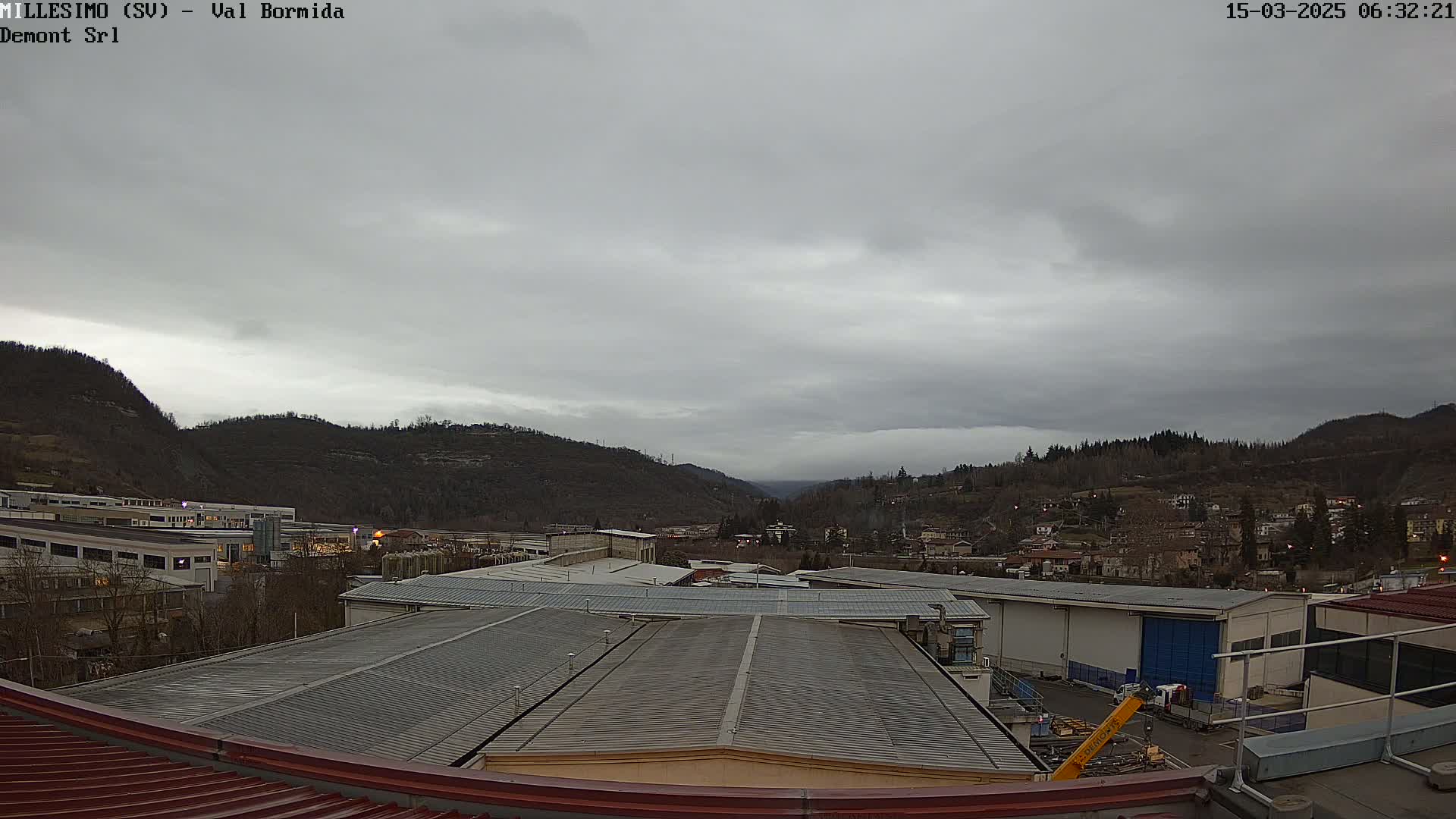 A view from a rooftop shows an overcast sky over industrial buildings and a valley nestled between hills.