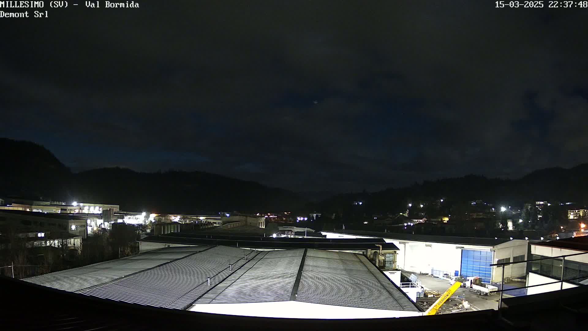 A nighttime view of an industrial area nestled between hills under a dark, cloudy sky.