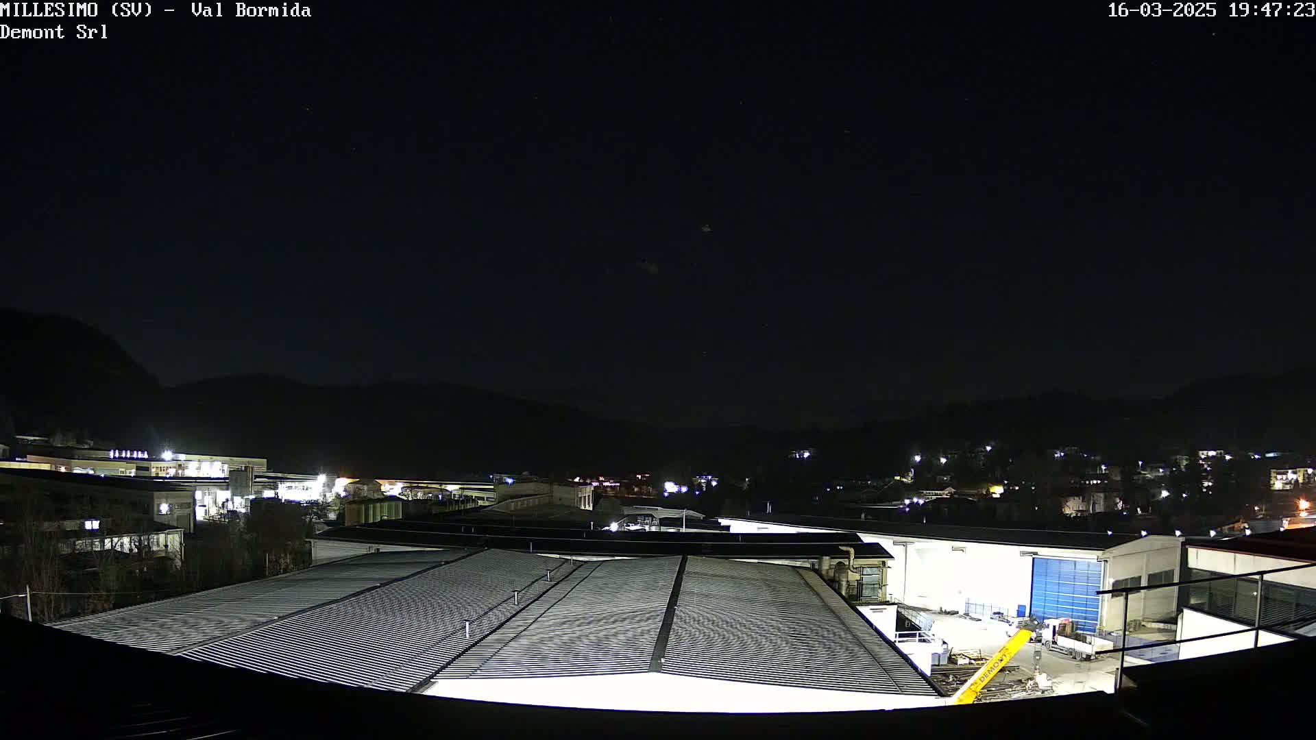 A nighttime view of industrial buildings and a small town nestled in a valley under a clear, starry sky.