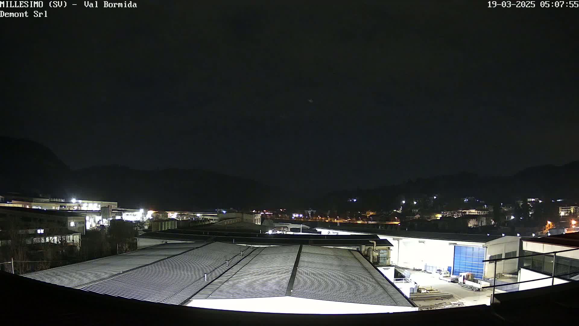 A nighttime view of an industrial area nestled against a dark mountain range under a clear, dark sky.