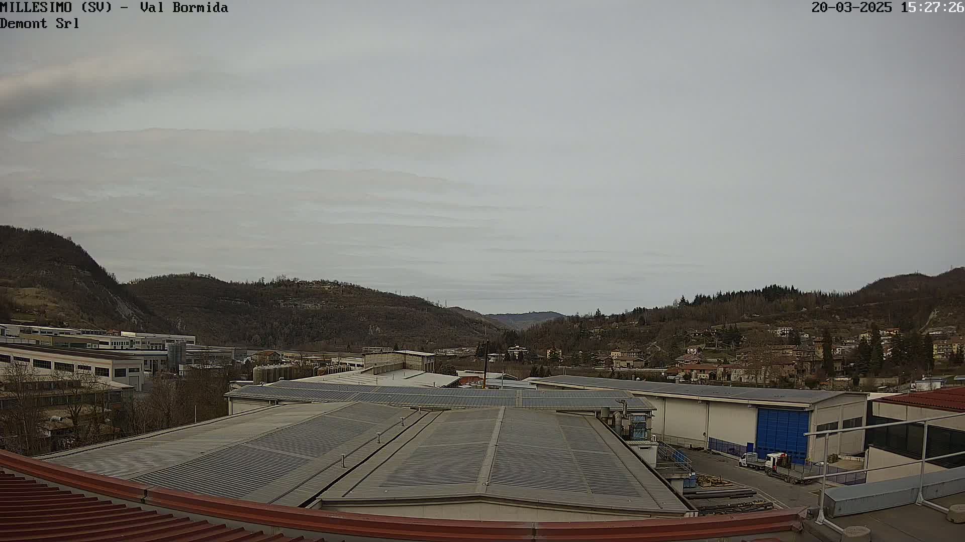 An overcast sky over an industrial area nestled in a valley between hills.
