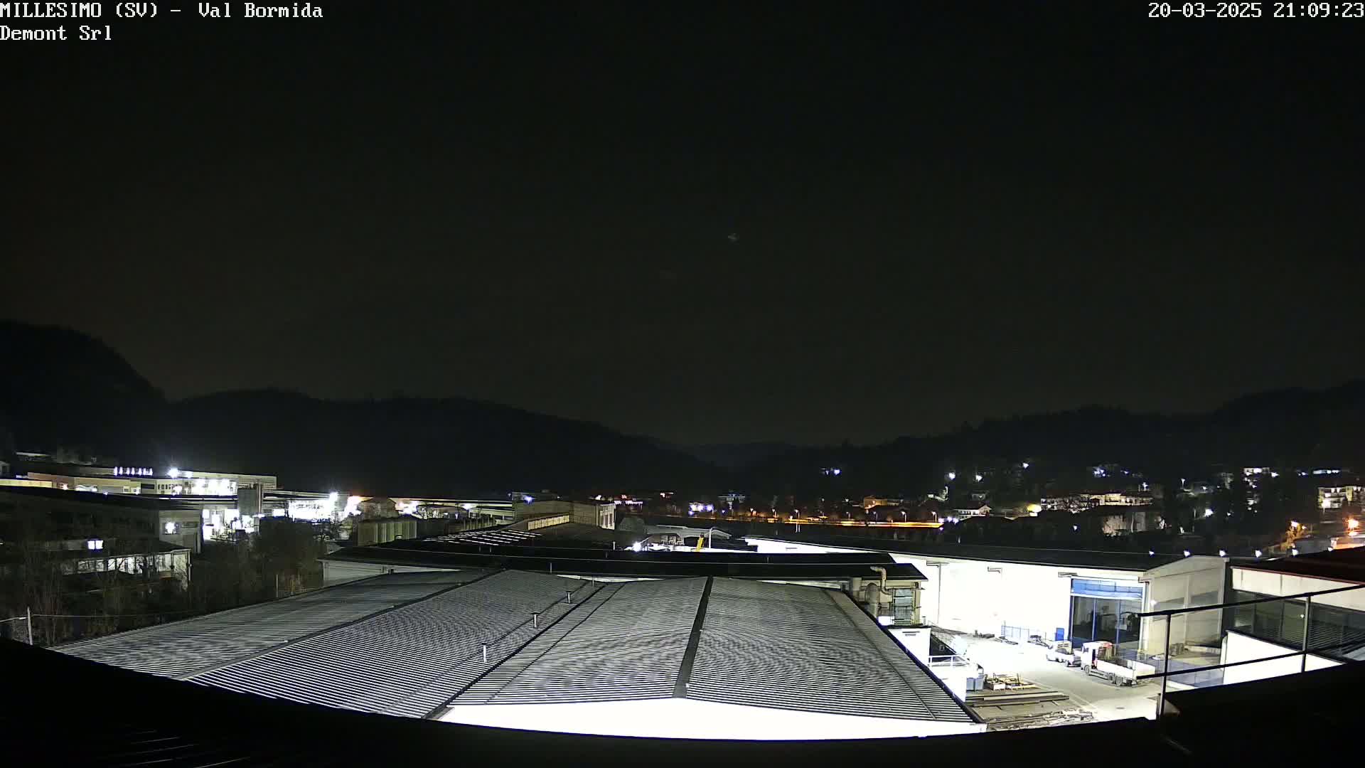 A nighttime view of an industrial area nestled against dark hills under a clear, dark sky.