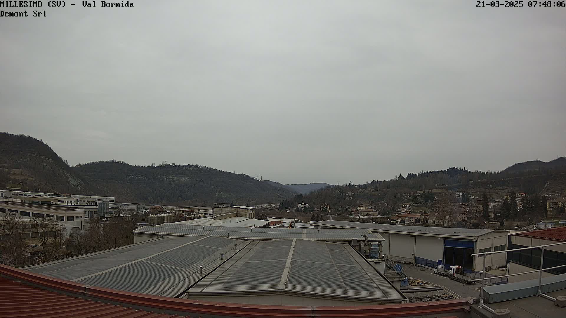 A view from a rooftop shows overcast skies, industrial buildings, and hills in the distance.