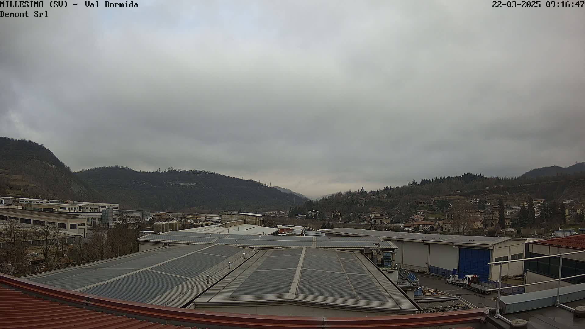 A view from a rooftop shows overcast skies over an industrial area nestled in a valley between hills.