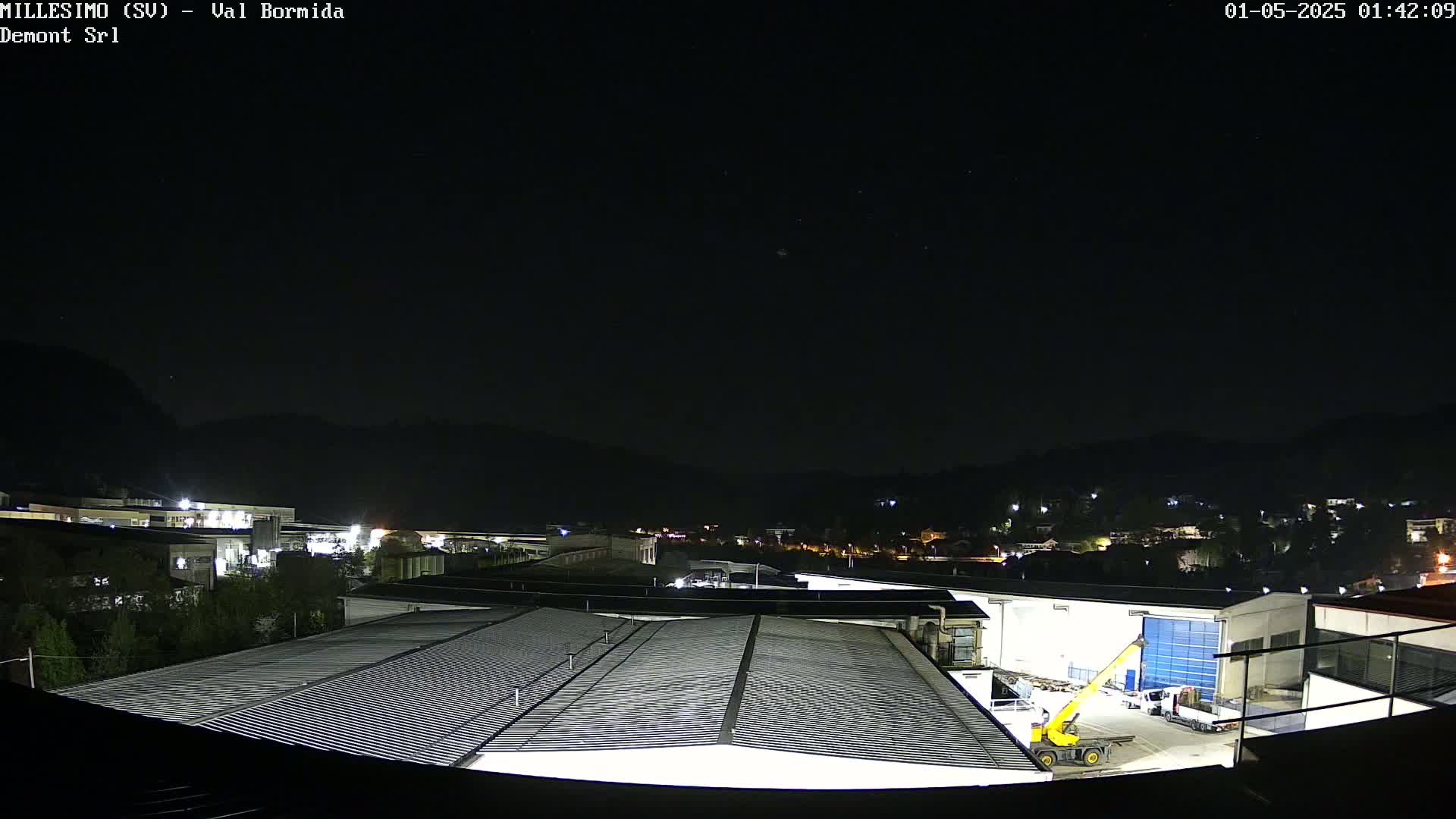 A nighttime view of an industrial area with a large corrugated metal roof in the foreground, under a clear, dark sky.