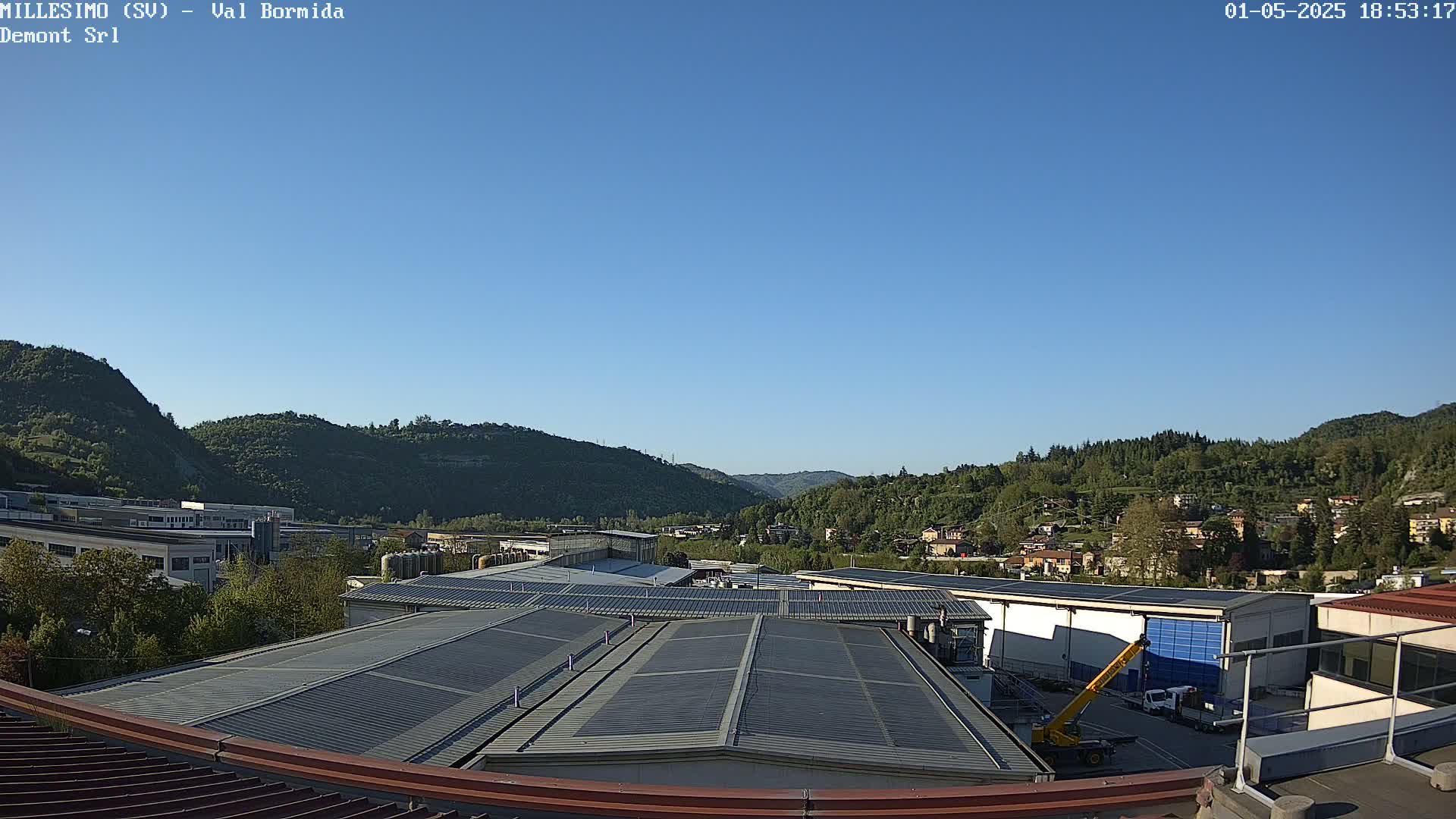 A clear blue sky over industrial buildings and green hills.