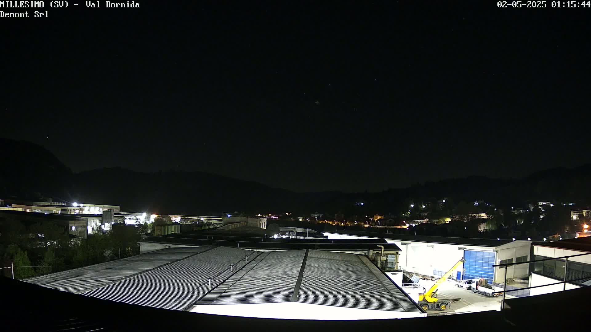 A nighttime view of industrial buildings and a small town nestled against dark hills under a clear, starry sky.