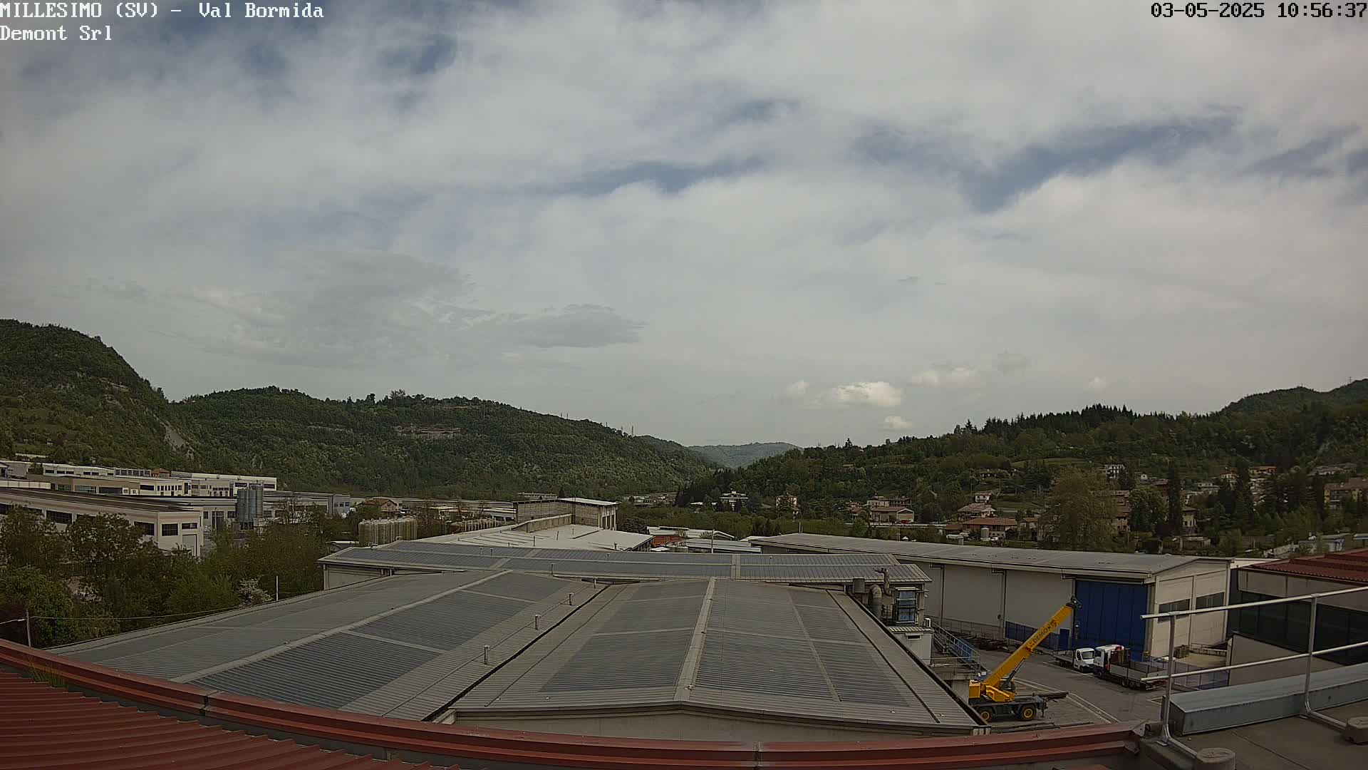 A view from a rooftop shows a cloudy sky over green hills and industrial buildings, with a yellow crane visible in the foreground.