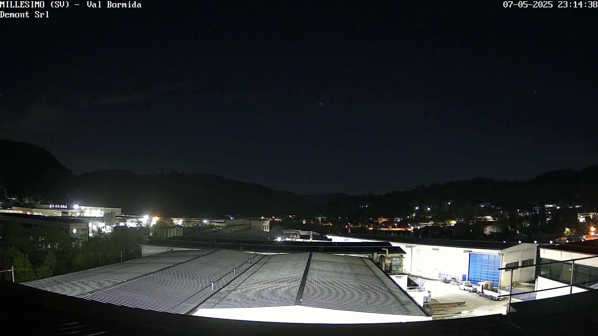 A nighttime view of a corrugated metal roof overlooking a small town nestled in a valley under a clear, starry sky.