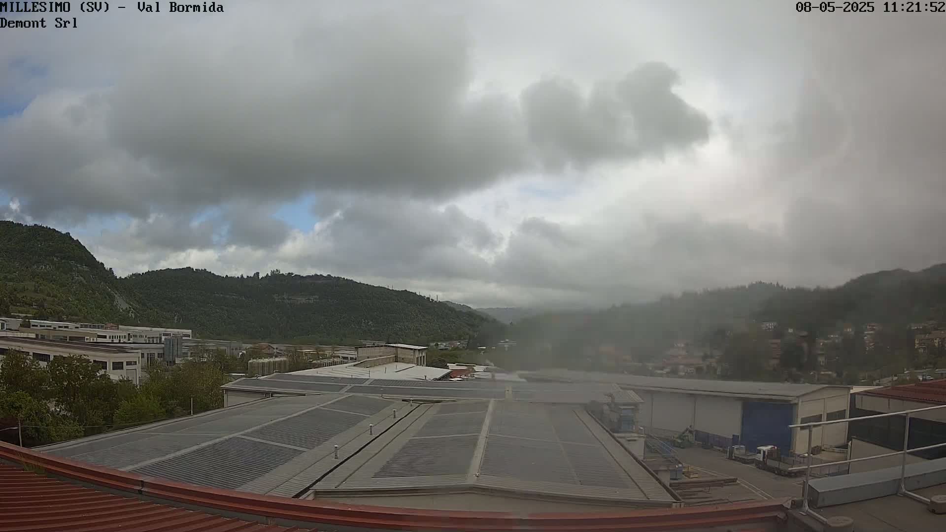 Overcast skies cover a valley with industrial buildings and green hills in the background.