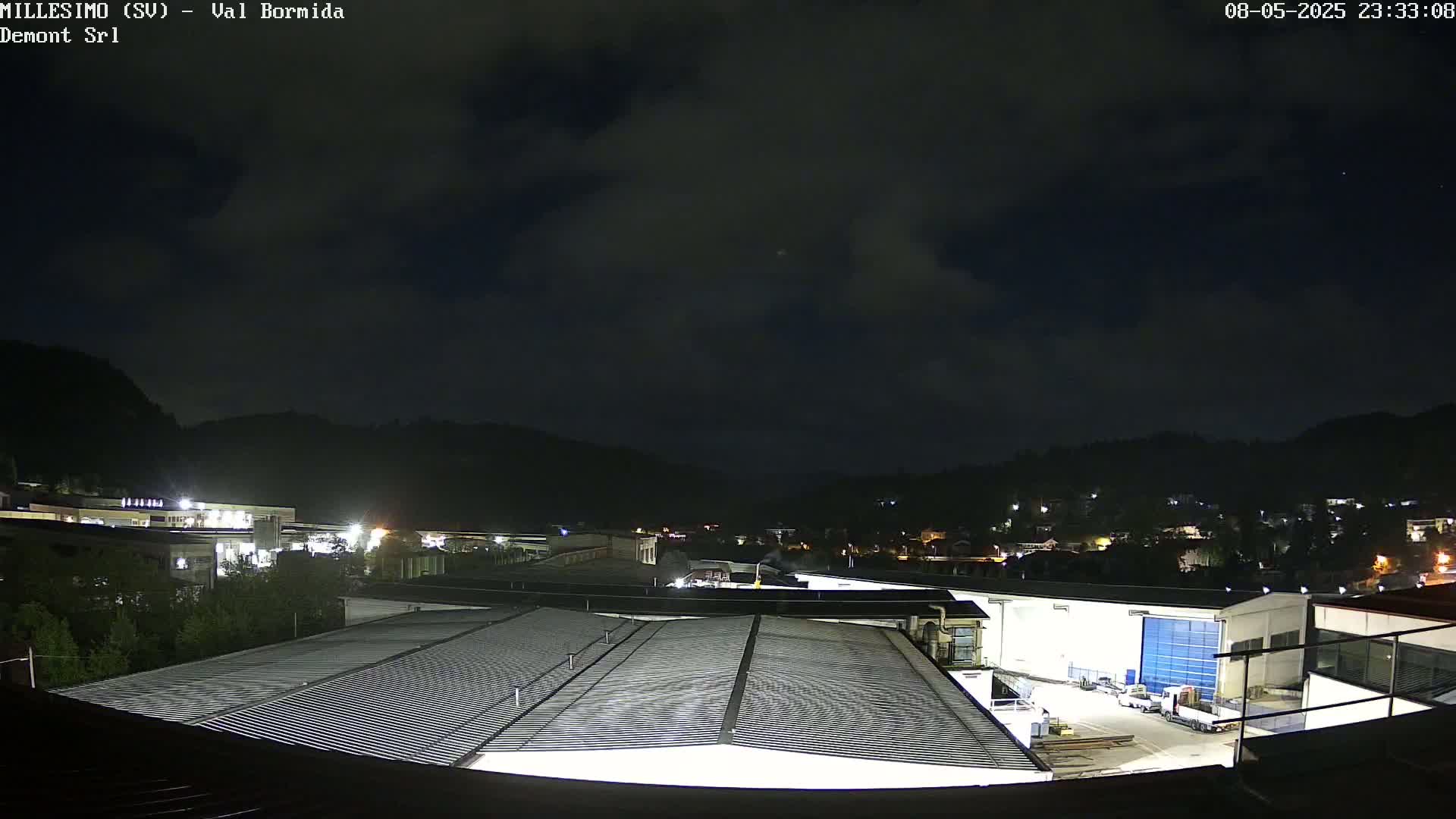 A nighttime view of an industrial area nestled in a valley under a cloudy sky.