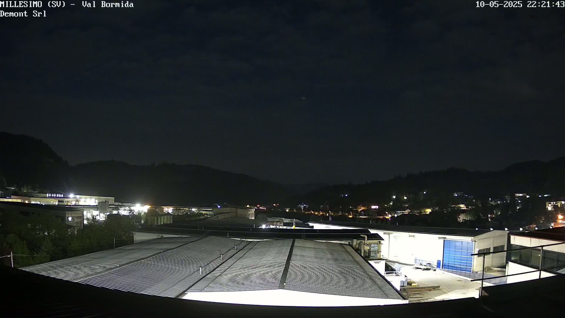 A nighttime view of an industrial area nestled against dark hills under a mostly clear sky.