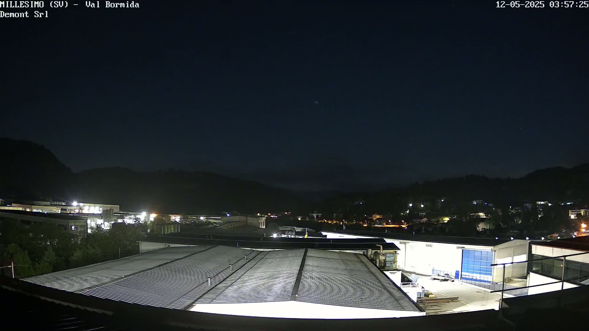 A nighttime view of a factory complex and surrounding town nestled in a valley under a clear, dark sky.