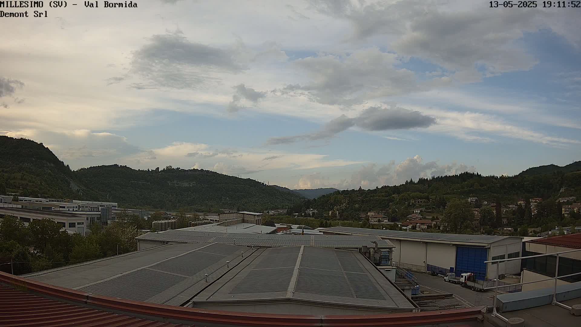A view from a rooftop shows a partly cloudy sky over a valley of green hills and industrial buildings.