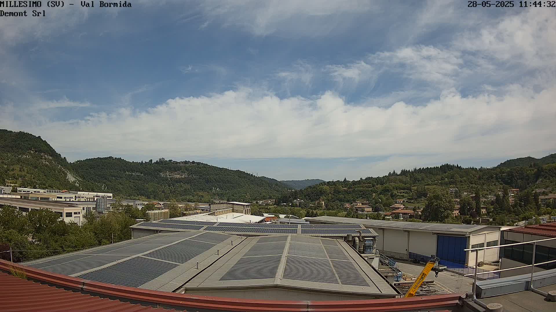 A mostly sunny day reveals a view of a valley with industrial buildings and residential homes nestled among tree-covered hills.