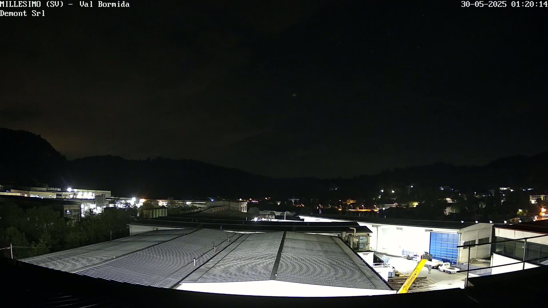 A nighttime view of a factory complex nestled in a valley under a clear, dark sky.