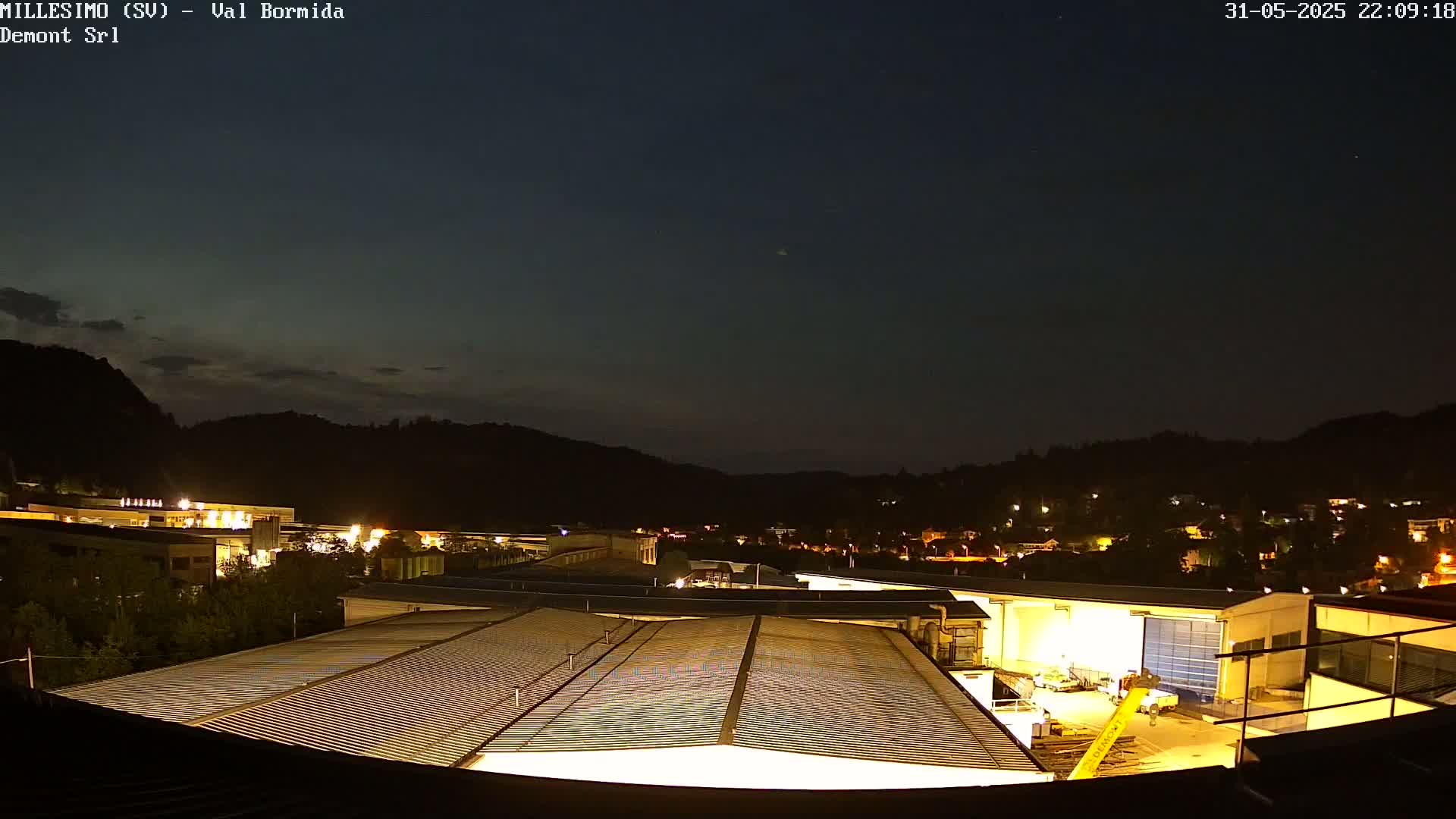 A nighttime view of a factory complex and a small town nestled in a valley under a dark, clear sky.