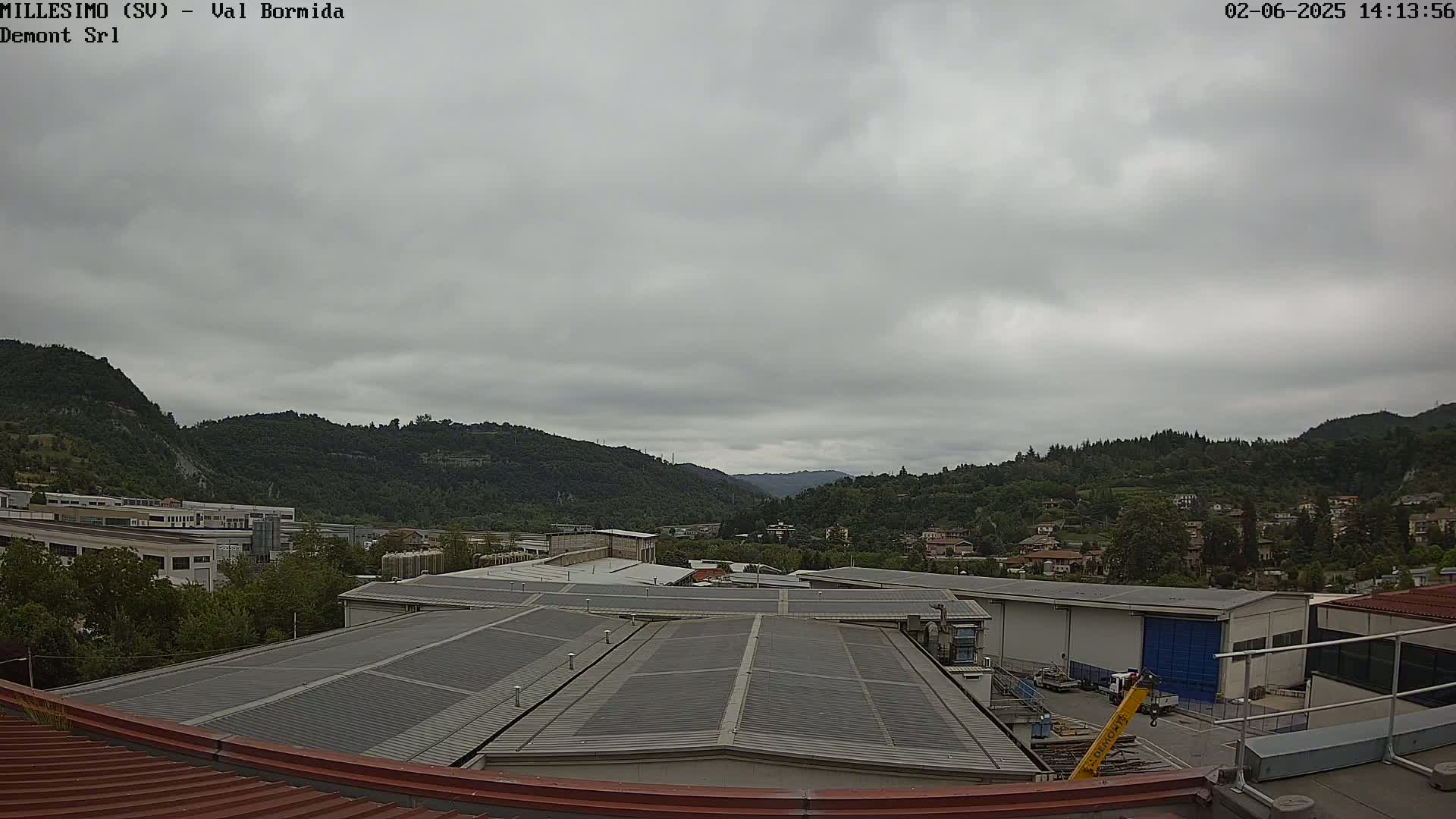 A view from a rooftop shows overcast skies over a valley filled with green hills, trees, and industrial buildings.
