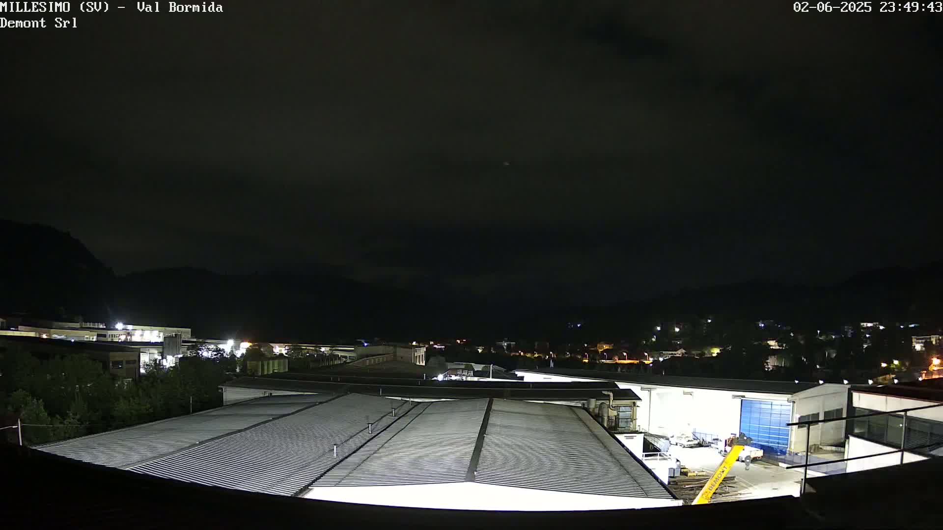 A nighttime view of an industrial area with buildings and a corrugated metal roof in the foreground, under a dark, clear sky.
