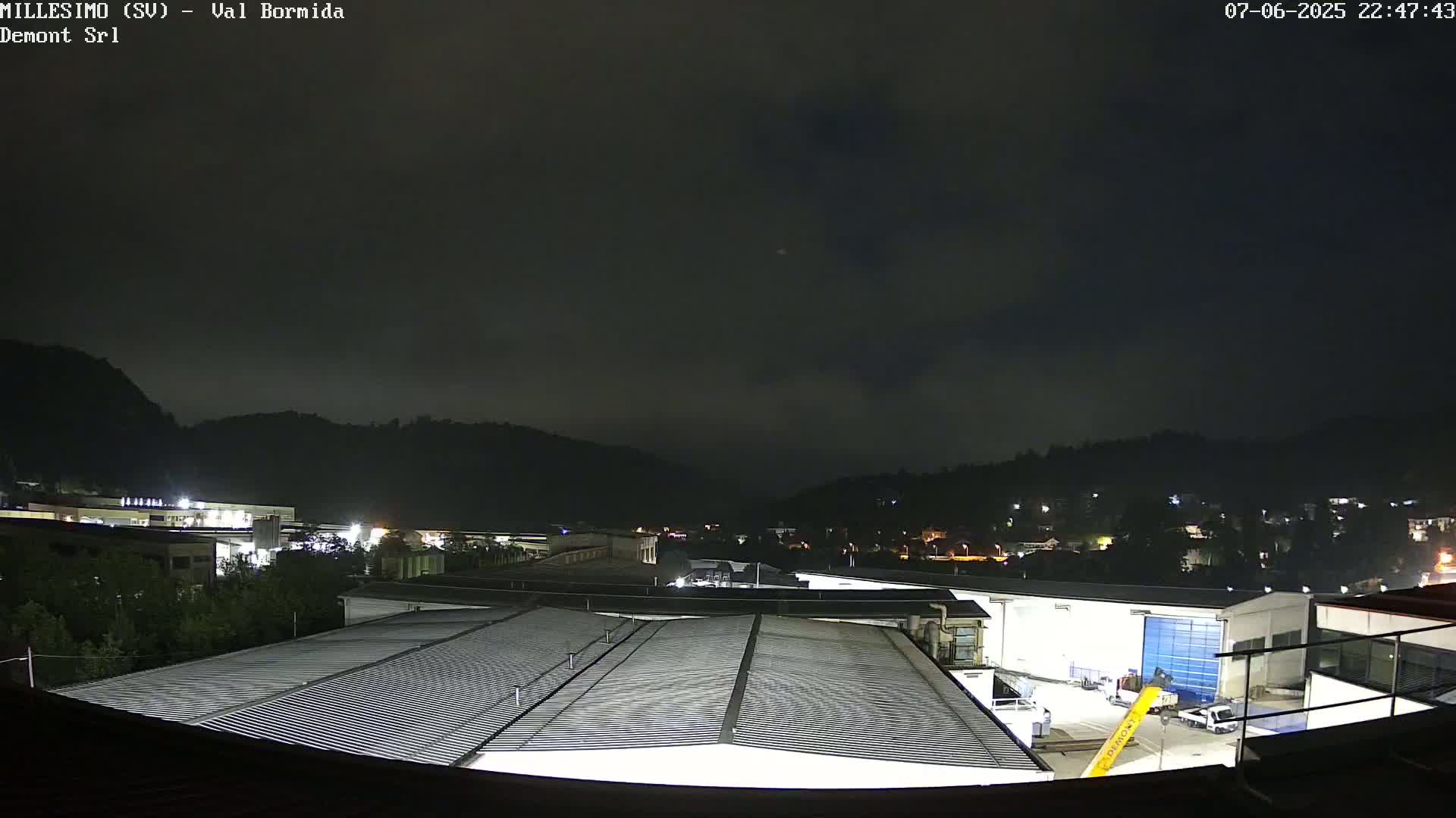 A nighttime view of an industrial area nestled in a valley, under a dark, cloudy sky.