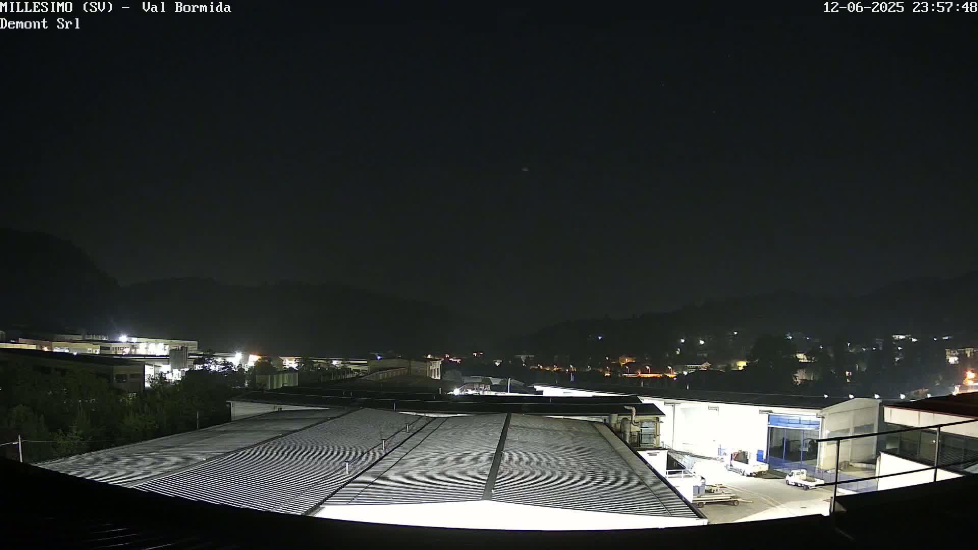 A nighttime view of an industrial area with a corrugated metal roof in the foreground, under a clear, dark sky.