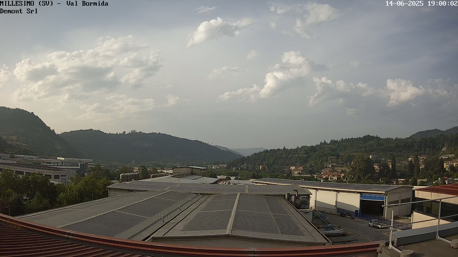 A partly cloudy sky overlooks an industrial area nestled in a valley surrounded by hills.