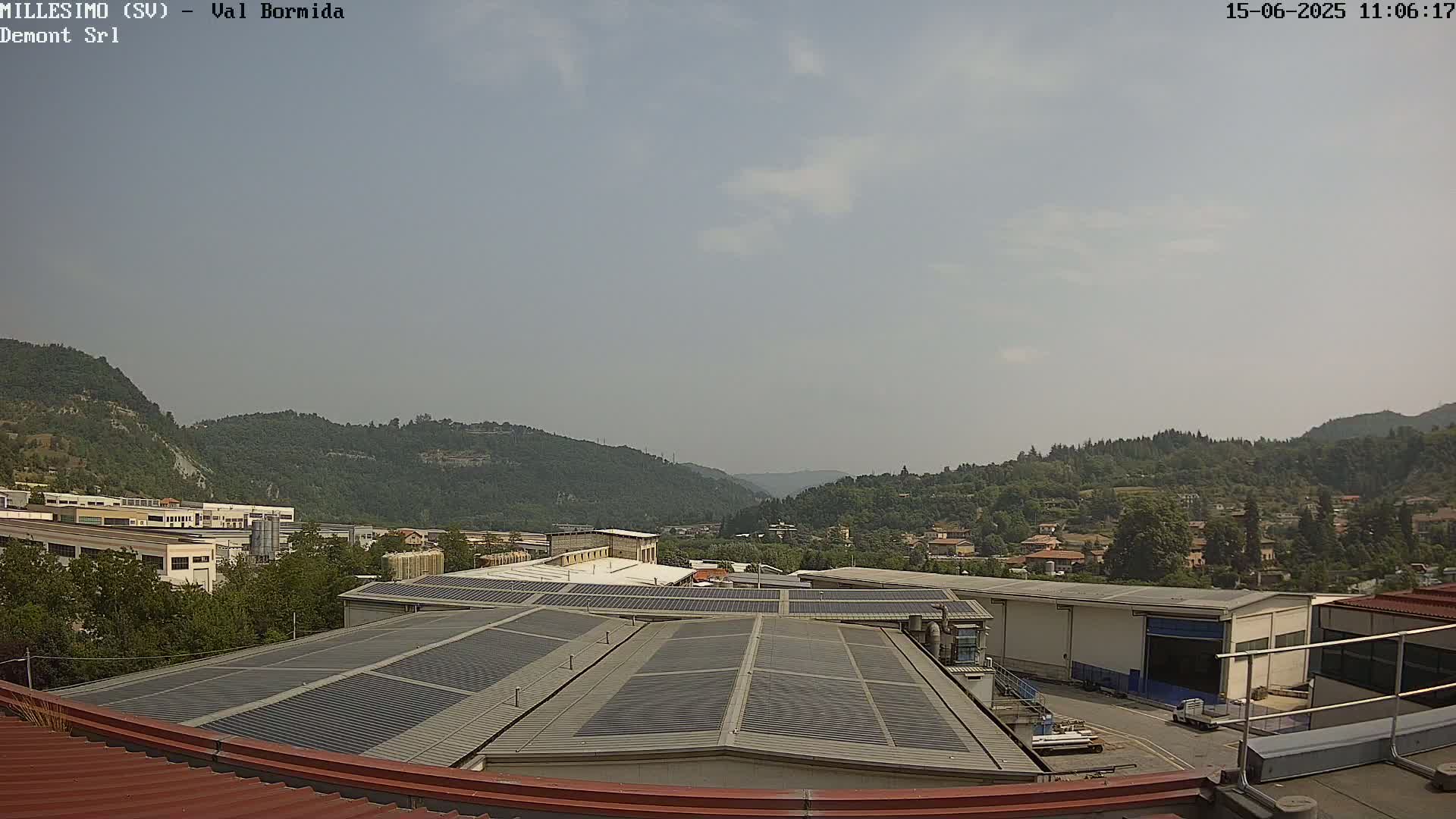 A view from a rooftop shows a hazy sky over a valley of green hills and industrial buildings with solar panels.