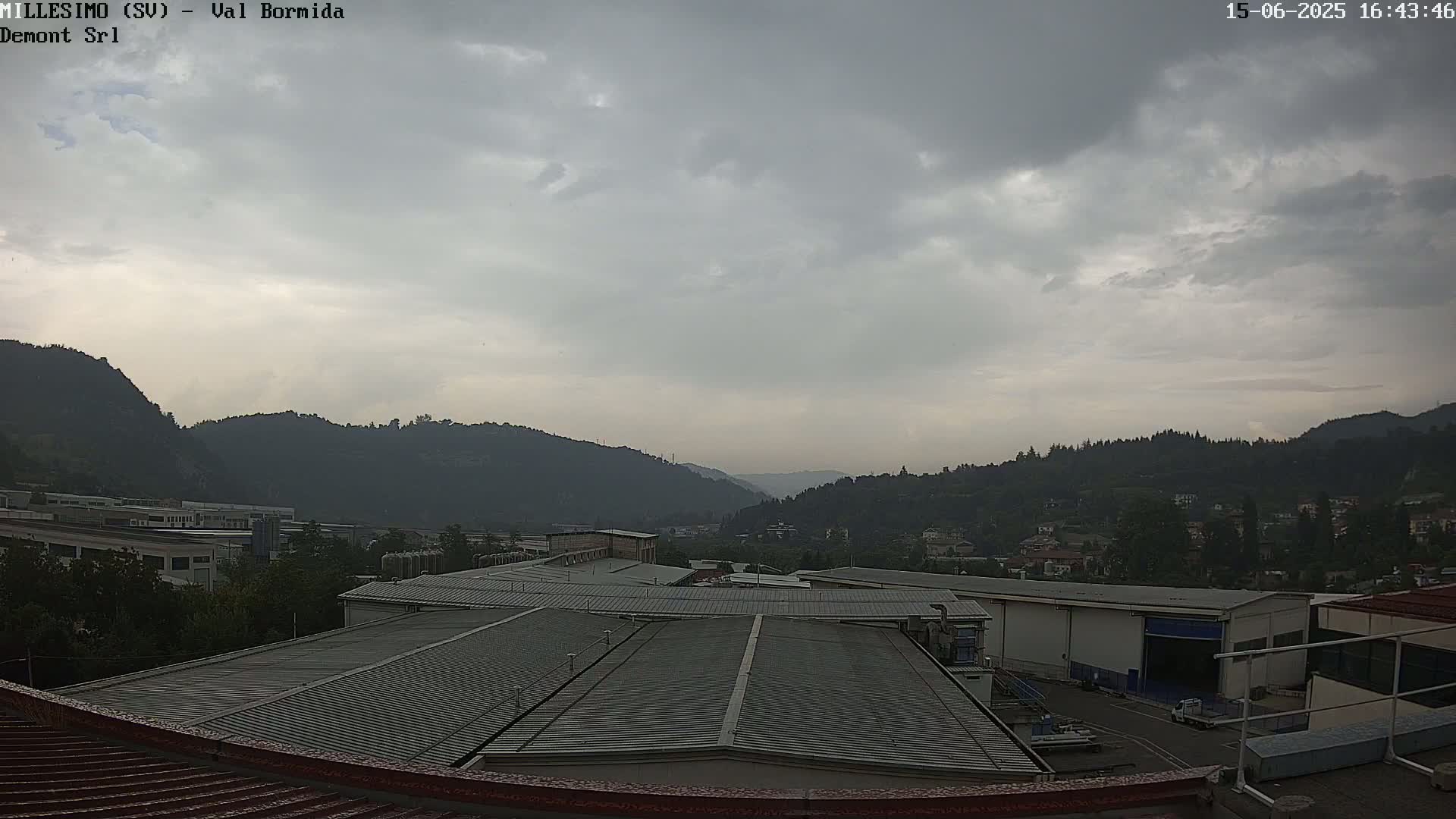 Overcast skies loom over a valley view of industrial buildings and distant hills.