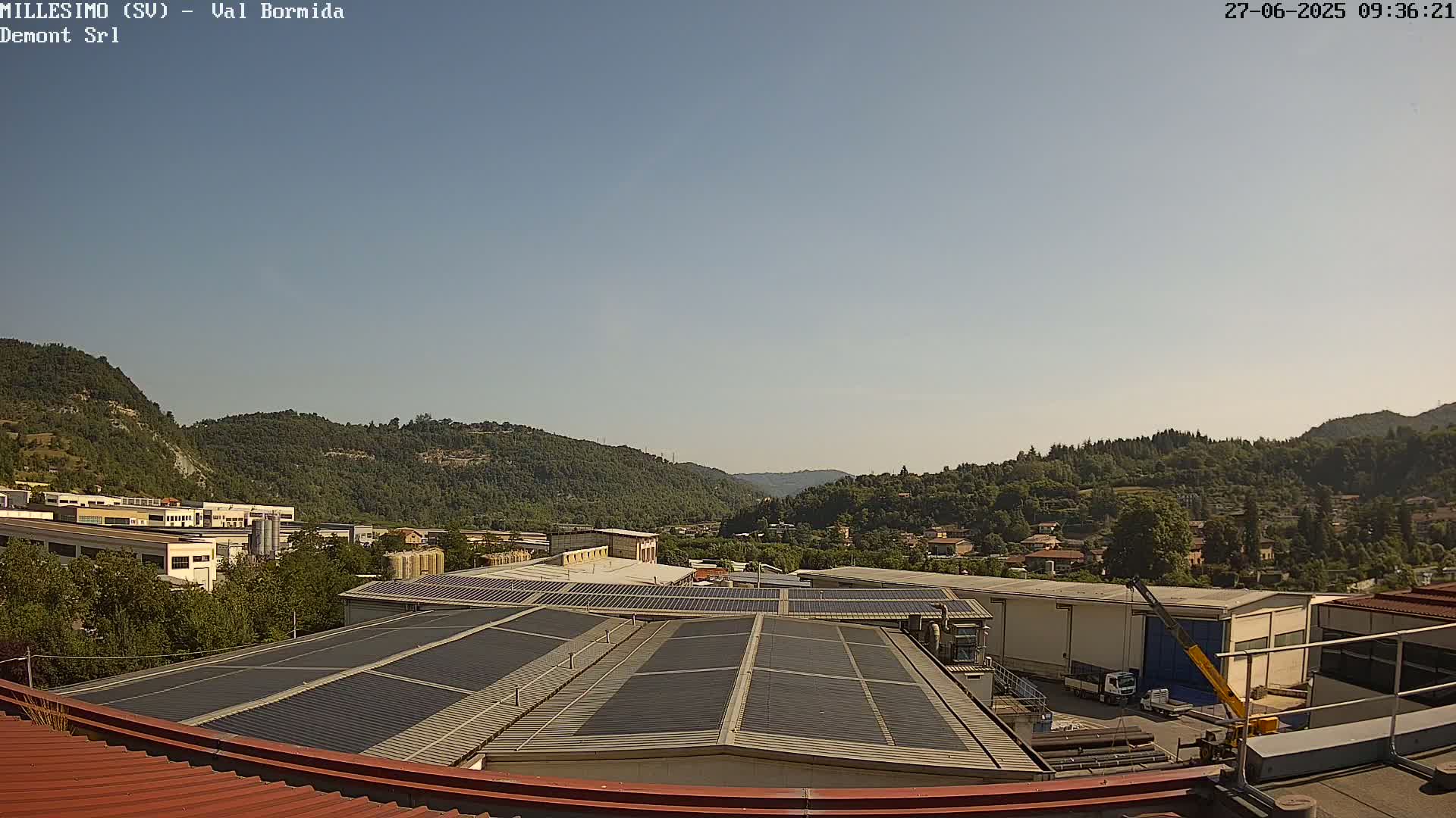 A view from a rooftop shows a clear sky over green hills and industrial buildings with solar panels.
