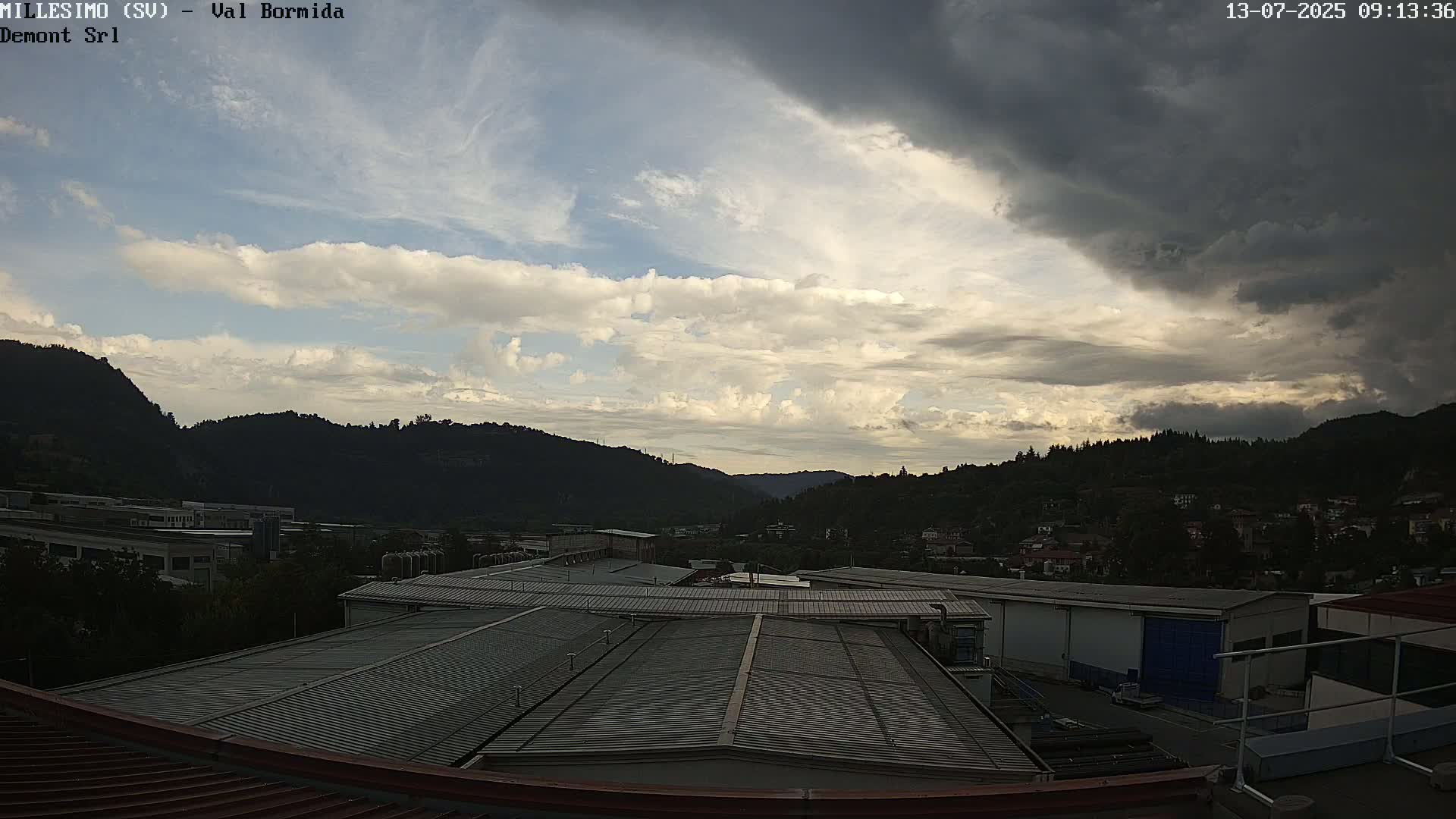A partly cloudy sky over a valley with industrial buildings and distant hills.