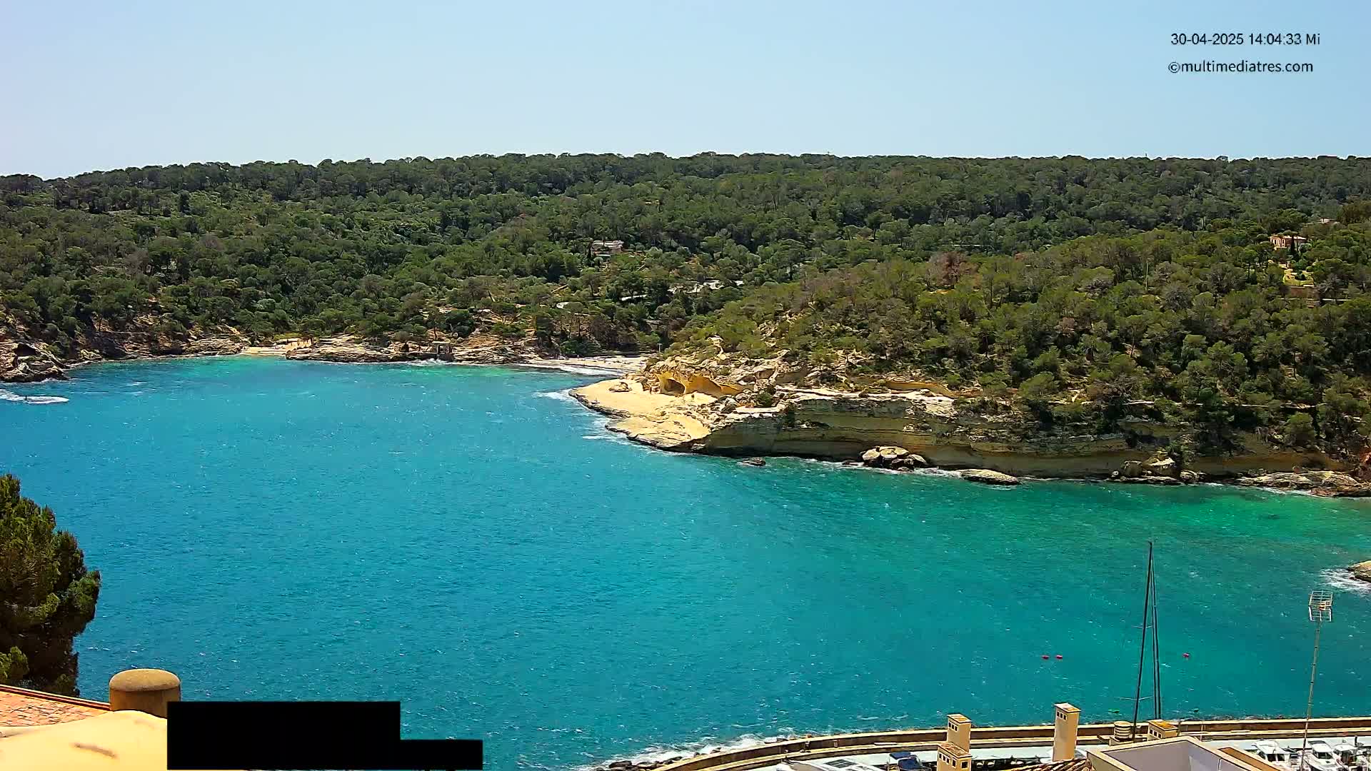 A bright, sunny day reveals a secluded cove with turquoise water, a small sandy beach, and lush green hillsides.