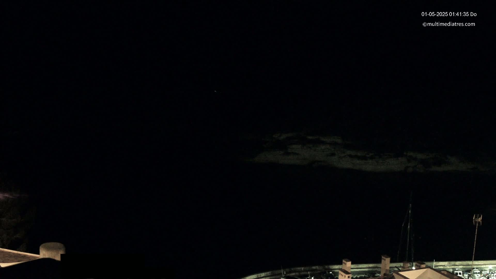 A dark, nighttime scene shows a body of water with a dimly lit shoreline and structures in the lower right corner.
