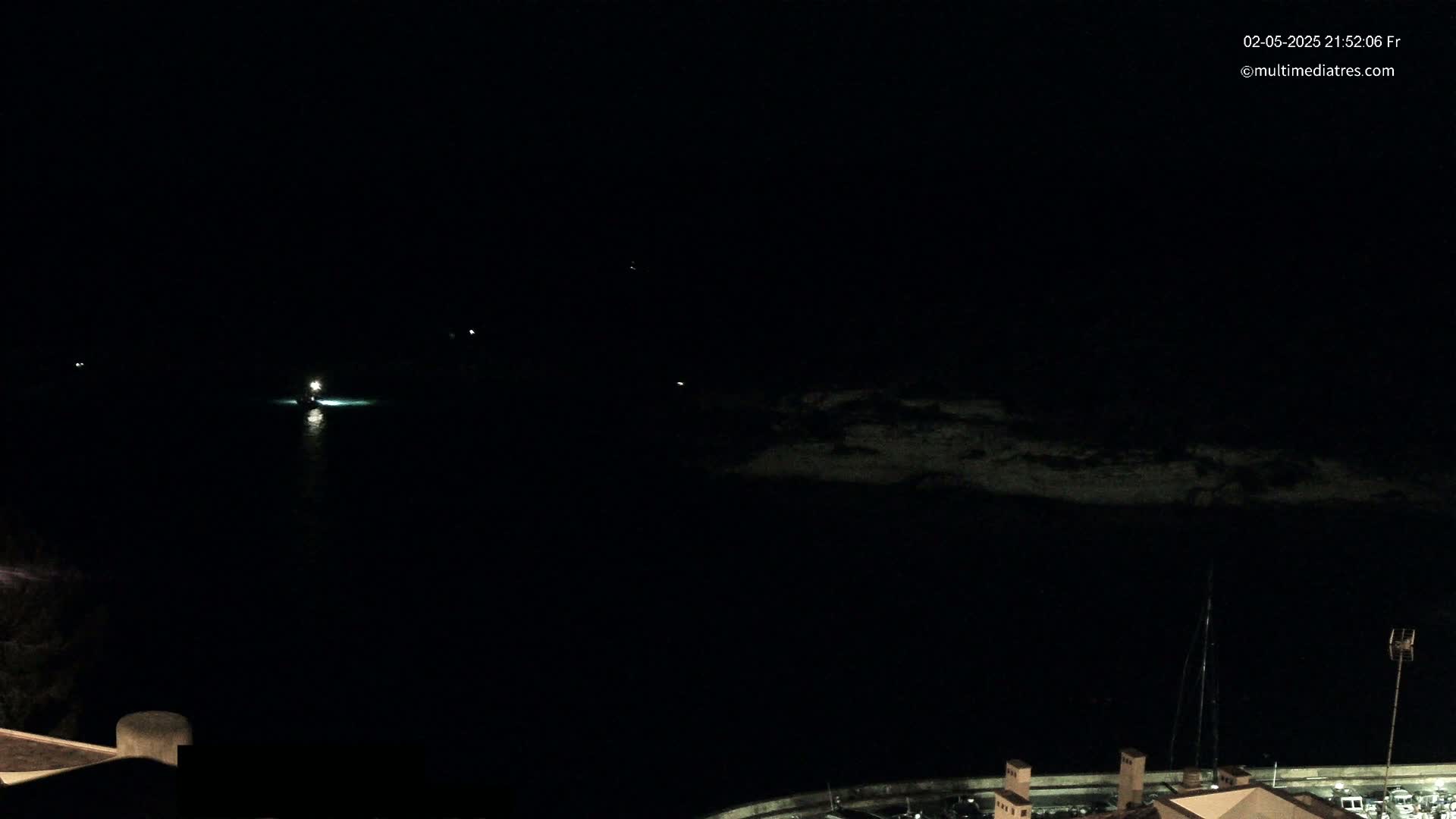 A nighttime, dark view of a body of water shows a few small lights on the water and a dark shoreline in the distance.