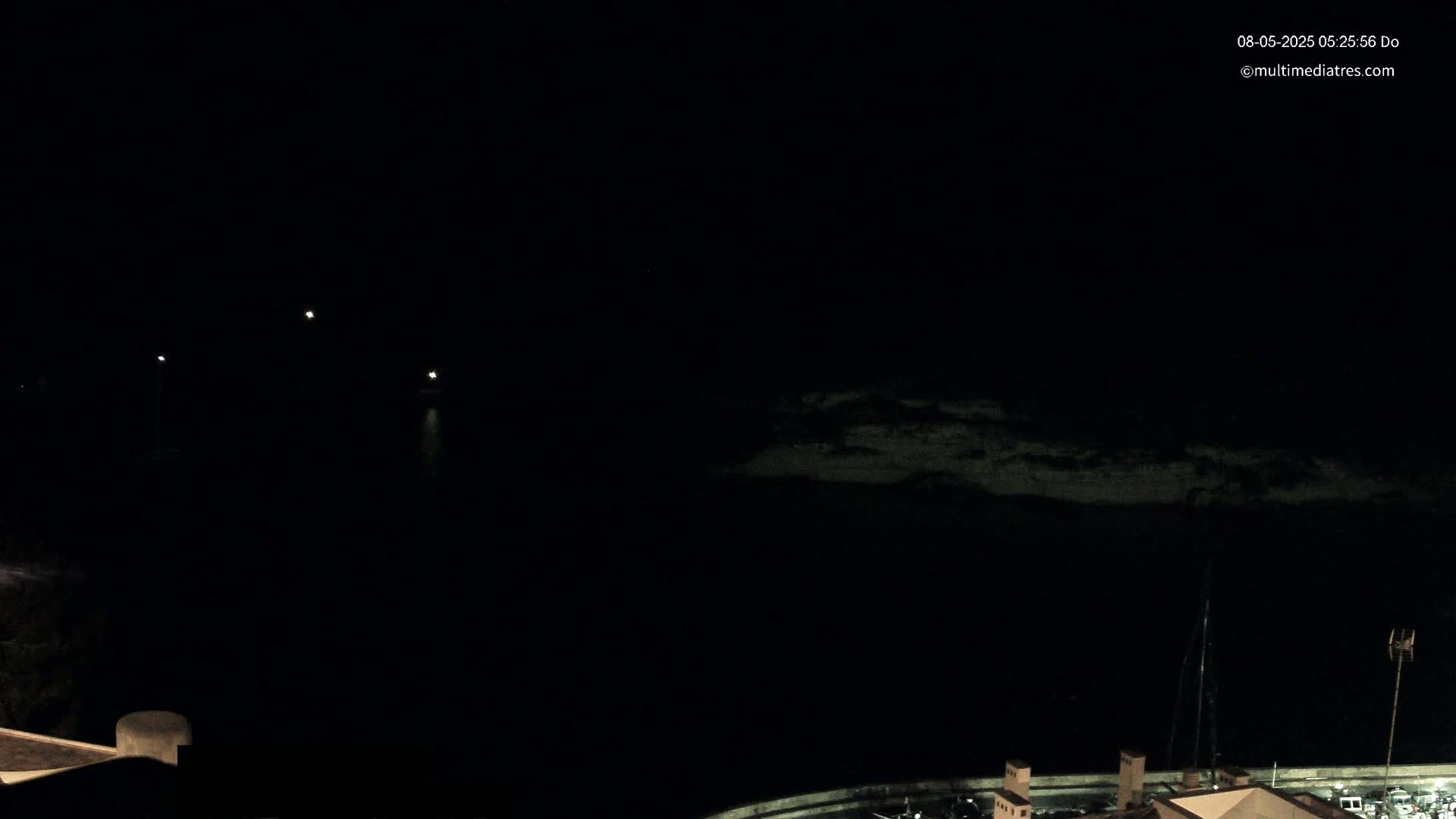 A nighttime, dark view of a body of water with dimly lit land in the background and a few faint lights on the water.