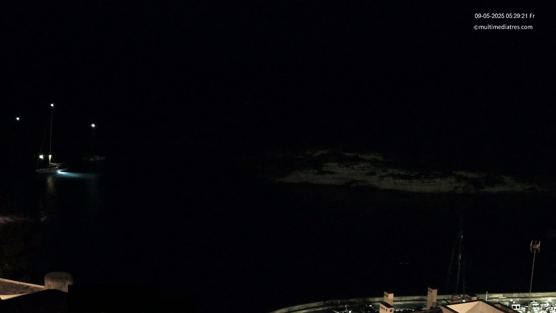 A sailboat is moored in dark water at night under a clear, dark sky illuminated by several lights.