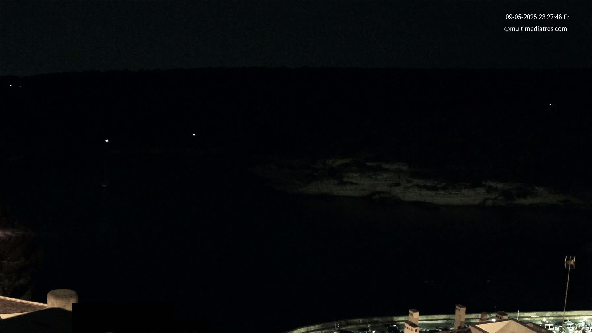 A nighttime, dark view of a body of water with a distant shoreline and a few faint lights visible in the distance.