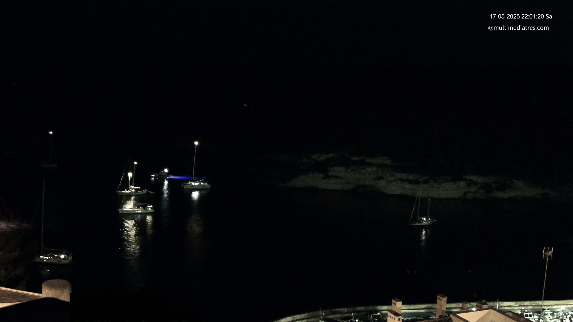 Several sailboats are moored in a dark, calm harbor at night.