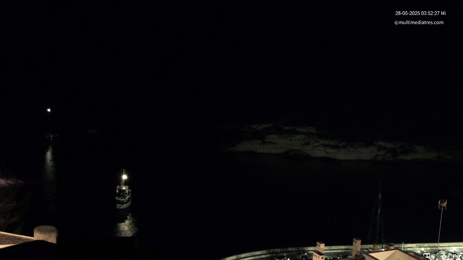 A small boat is illuminated on dark water at night near a dimly lit shoreline.