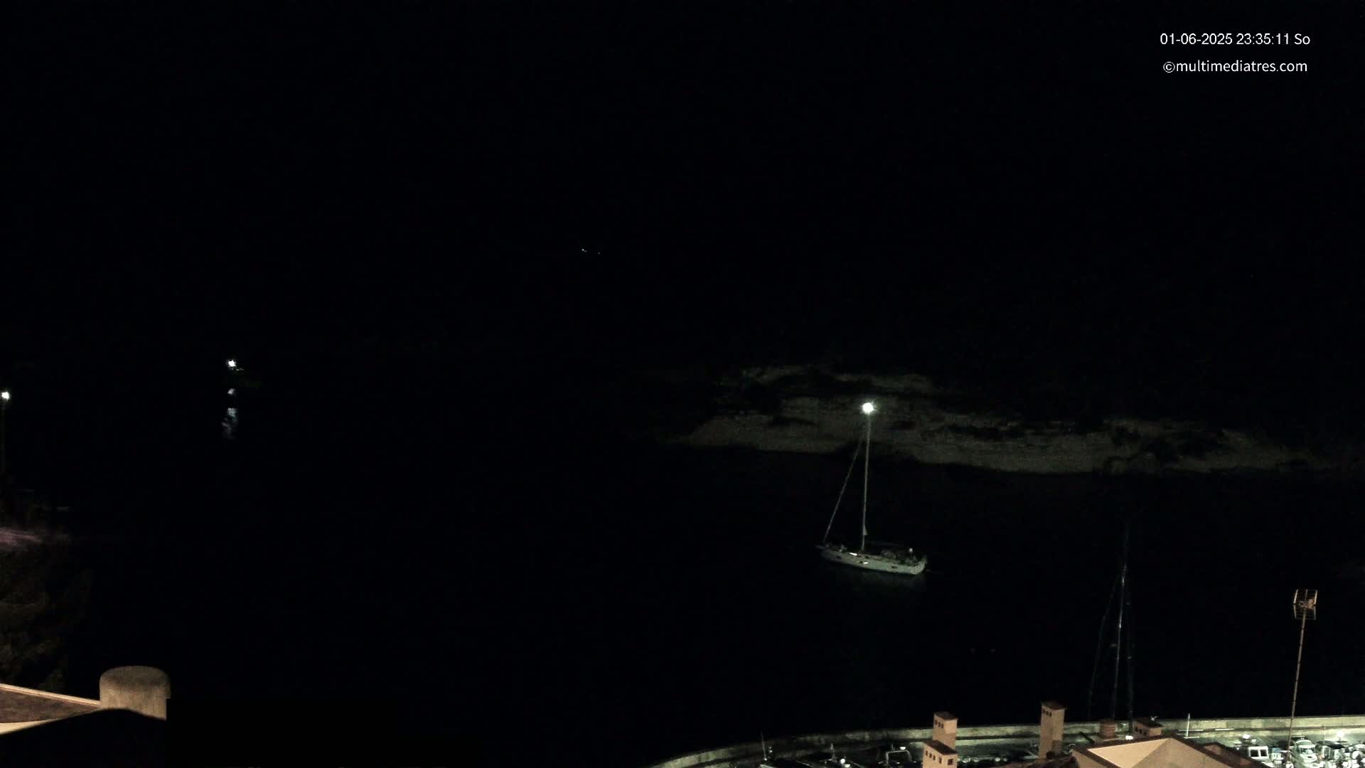 A sailboat is moored in a dark, calm body of water at night.