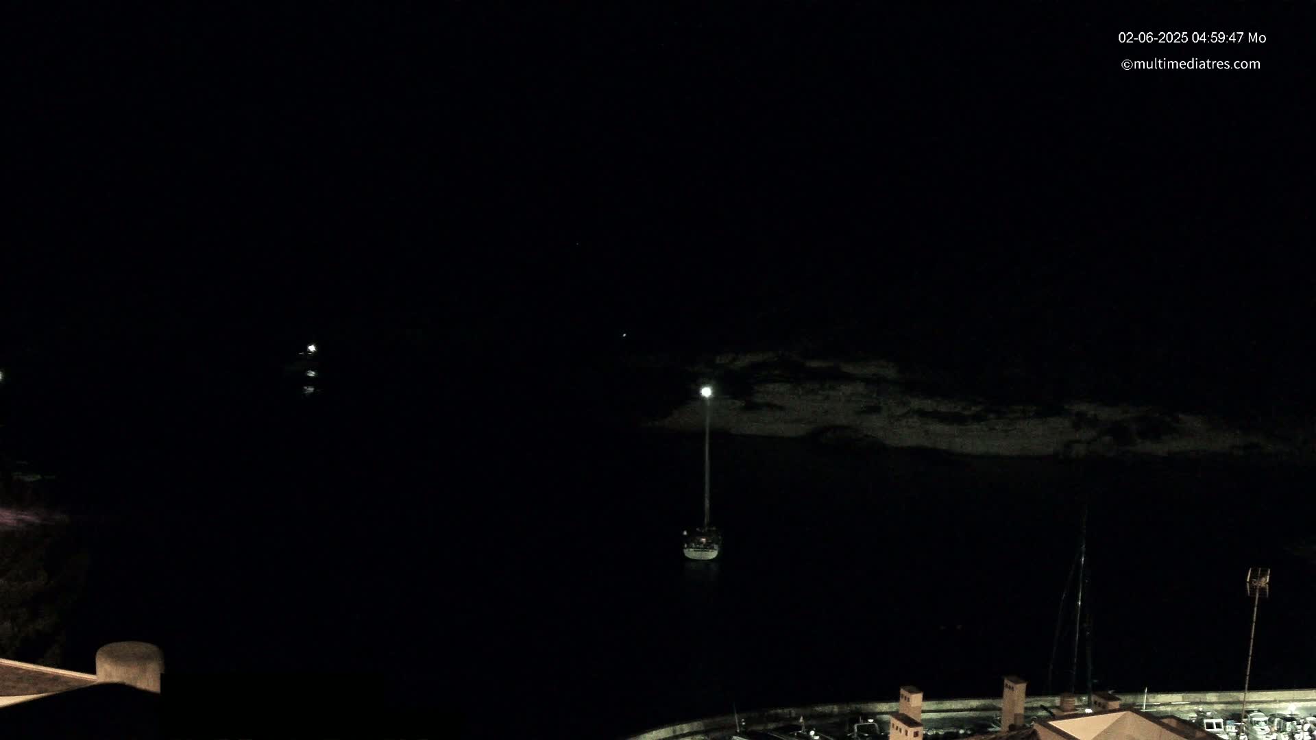 A sailboat is moored in a dark, nighttime harbor.