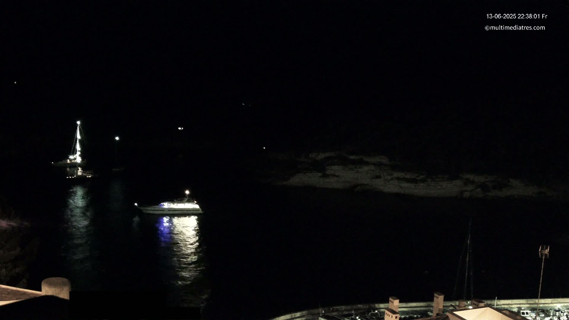 Two boats are illuminated at night on dark water near a rocky shoreline.