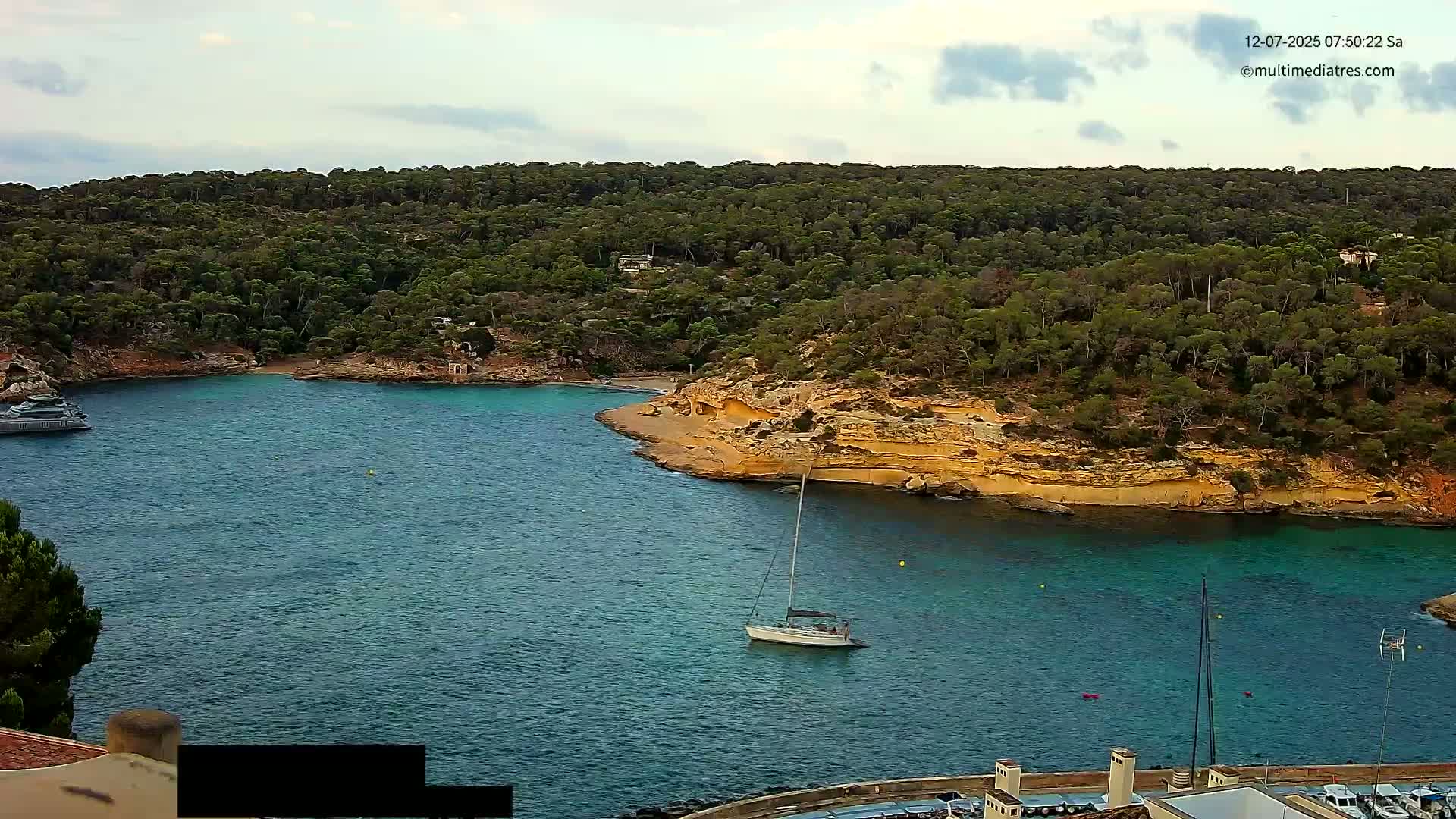 A secluded cove with turquoise water is surrounded by a lush, green hillside under a cloudy sky.