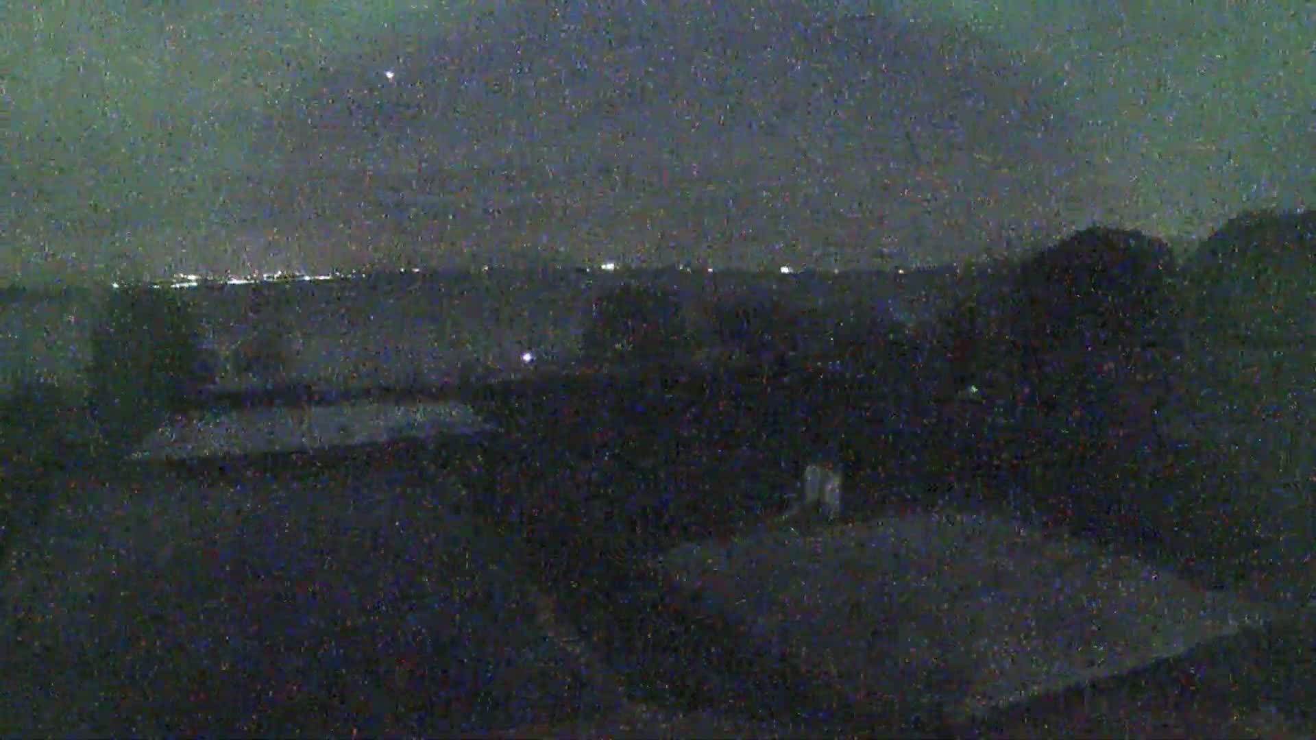 A nighttime, low-light view shows a dark landscape with a distant, faintly lit horizon.