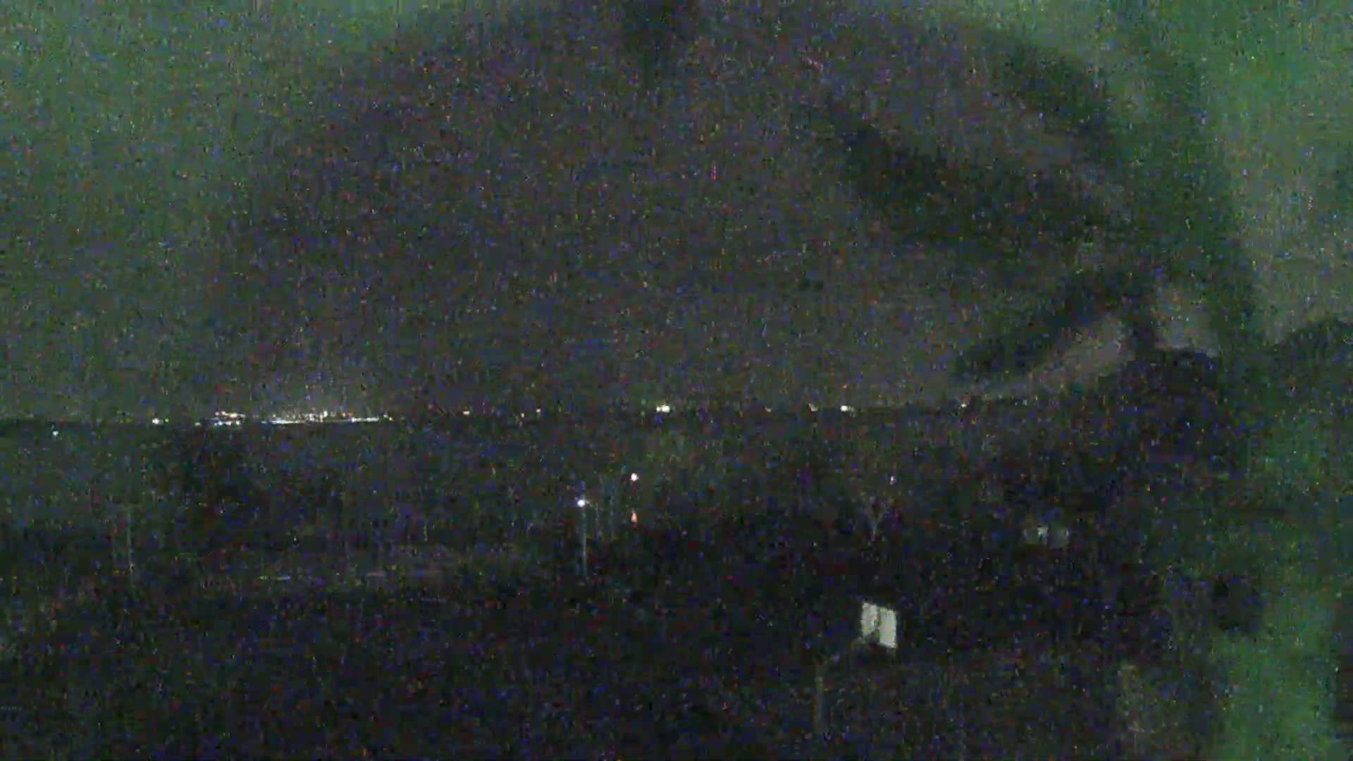 A nighttime long shot shows a dark, possibly overcast sky above a dimly lit landscape with a distant city skyline faintly visible on the horizon.