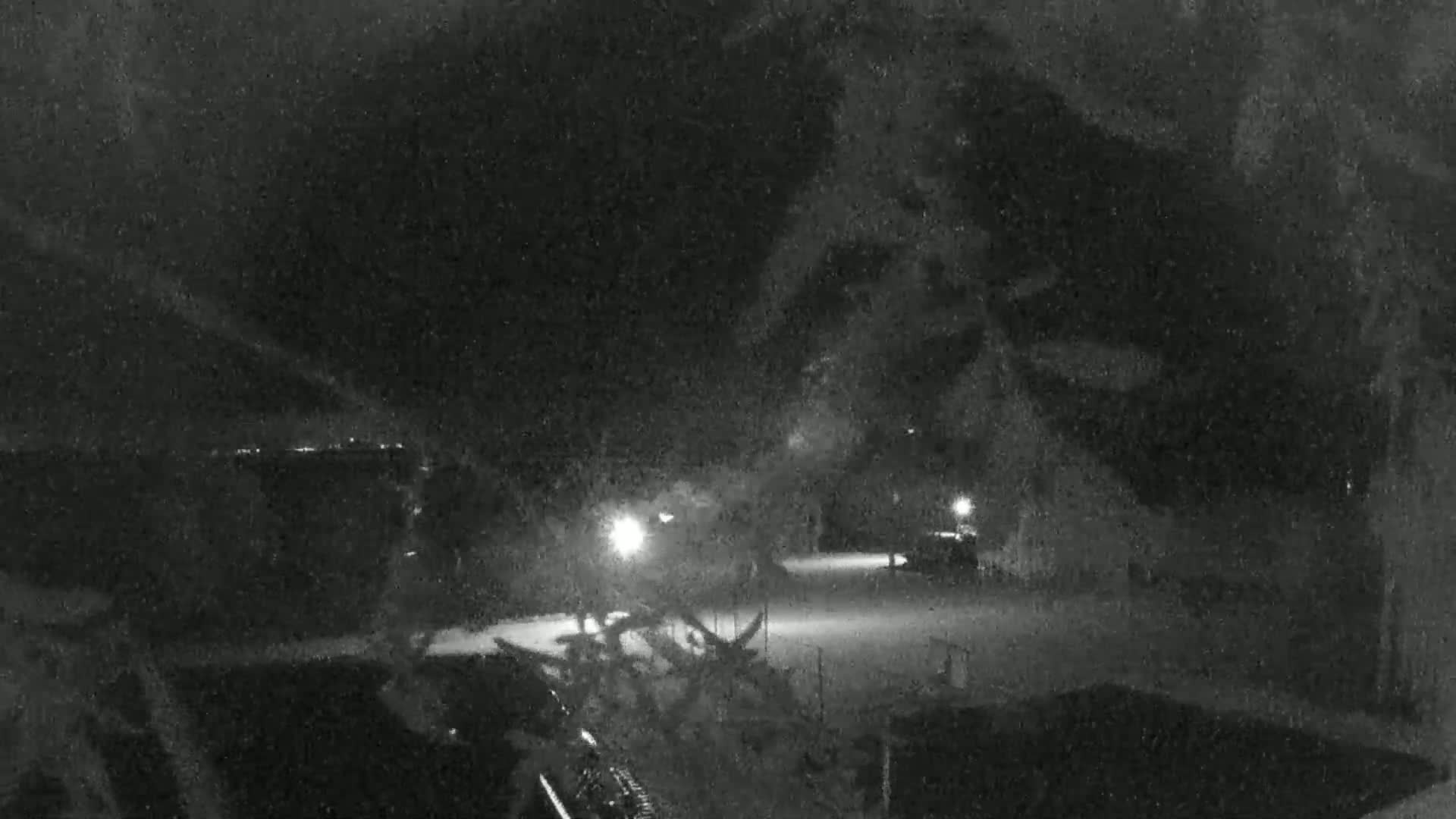 A nighttime snow-covered scene shows a dimly lit area with vehicles and trees, viewed through a snowy foreground.