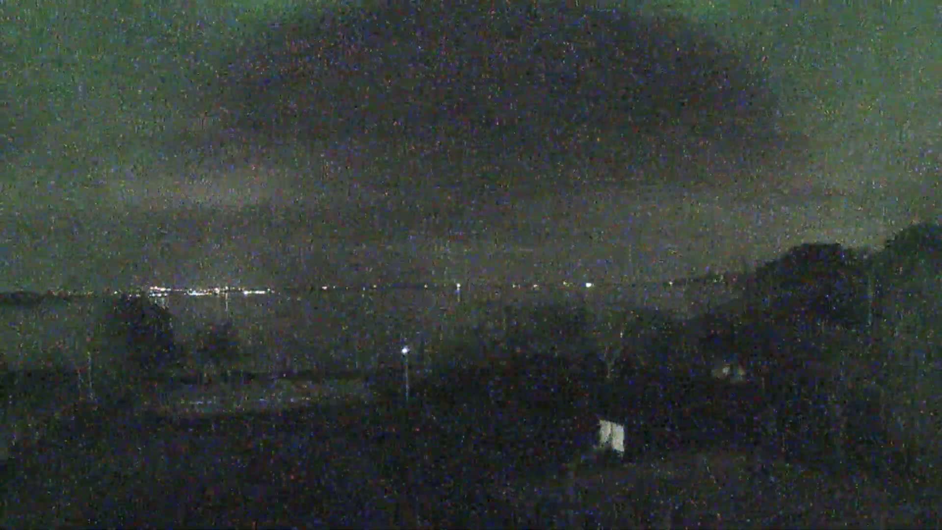 A nighttime view of a body of water with distant city lights under a dark, cloudy sky.