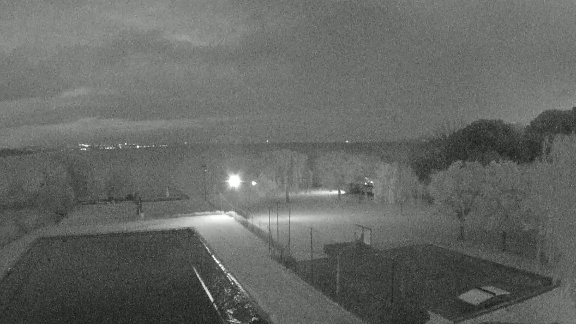 A nighttime, low-light view shows an empty sports court and swimming pool area, with a dimly lit horizon in the background.