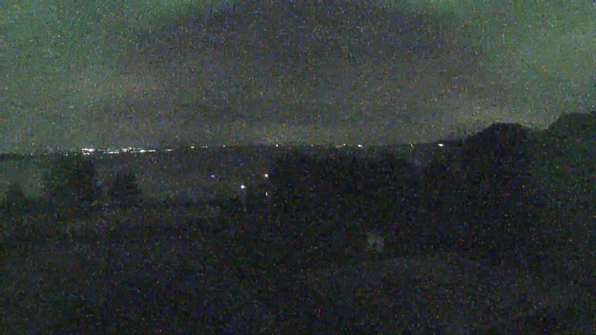 A nighttime view of a distant city skyline under a dark, cloudy sky.